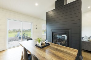 A modern interior with a wooden dining table, chairs, a fireplace, and a view of the outdoors. - Waves and Woods Vacation Rental (Lot 39)