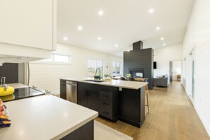 A modern kitchen with a central island, dark cabinetry, and a built-in oven. - Waves and Woods Vacation Rental (Lot 39)