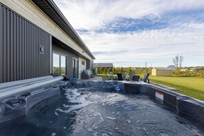 A hot tub area with a view of a house and a grassy yard. - Waves and Woods Vacation Rental (Lot 39)