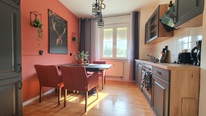 A modern kitchen with wooden cabinets, a dining area with red chairs, and a large window providing natural light.
