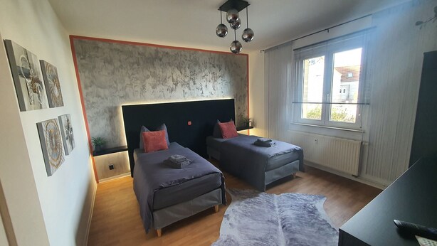 A bedroom with two beds, a large window, and a ceiling light fixture.
