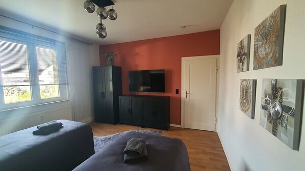 A room with a TV on a stand, a wardrobe, a bed, and artwork on the wall.