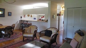 Un salon comprenant un coin repas, avec des meubles en osier, une machine à café et un réfrigérateur.