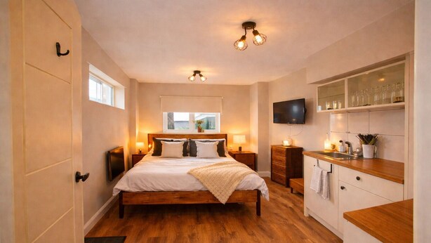 Un dormitorio con cama de madera, mesitas de noche, televisor y una cocina con lavabo y armarios.