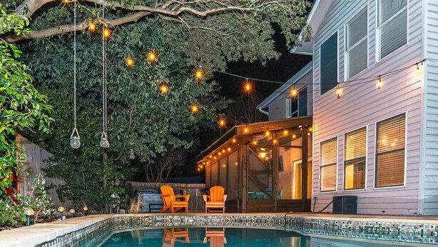 Ein Schwimmbecken mit Glasüberdachung, umgeben von einer Terrasse mit Liegestühlen und Lichterketten.