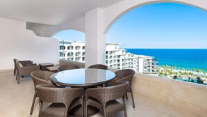 Una mesa redonda con sillas de mimbre en un balcón con vistas a una playa y edificios de hotel.
