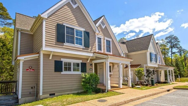 Une maison à deux étages avec un porche à l’avant, un garage et un petit jardin devant.