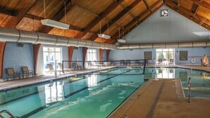 Une piscine intérieure avec des couloirs bien délimités, des chaises longues et un haut plafond en bois.