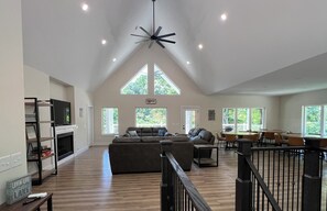 A spacious living area with a high ceiling, a fireplace, a large sofa, and a dining area with tables and chairs. - Brand New, Spacious 9 bedroom, 9 1/2 bath Waterfront house in Lakeside Estates (LaFollette)