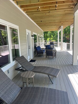 A covered deck with wicker furniture, a pergola, and a view of a wooded area.