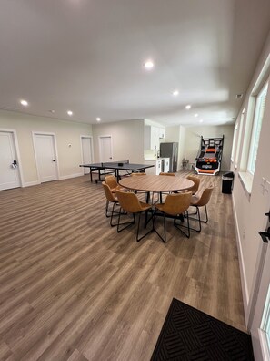 A spacious room with a ping pong table, a kitchen area, and a bed with a basketball theme.