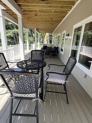 Eine überdachte Terrasse im Freien mit Tisch und Stühlen, weißen Geländern und großen Fenstern.
