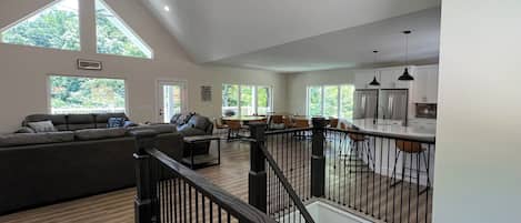 A spacious living area with a high ceiling, a staircase, and a kitchen area.