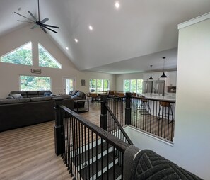 A spacious living area with a high ceiling, a staircase, and a kitchen area.