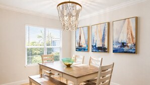 Une salle à manger avec une table en bois, des chaises, un lustre et des tableaux représentant des voiliers accrochés au mur.