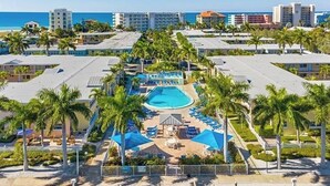Un complexe hôtelier doté d’une piscine centrale, de palmiers et offrant une vue sur l’océan.
