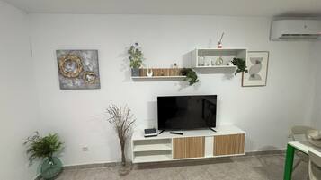 A modern living room with a flat-screen TV, white shelves, and decorative items.