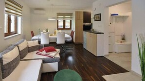 En moderne stue med sofa, spisebord og et køkken med skabe og et køleskab.
