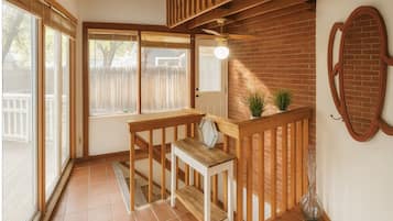 Ein Eckzimmer mit einer hölzernen Bank, einem kleinen Tisch, einem Deckenventilator und einer Backsteinwand.