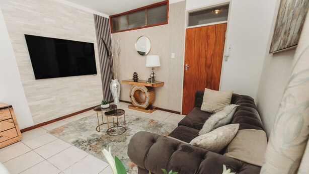 Ein Wohnzimmer mit einem braunen Sofa, einem Flachbildfernseher, einem Holztischchen, einem Spiegel und einer Tür.