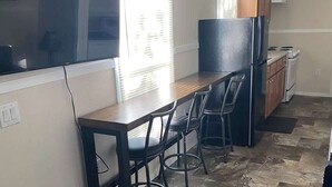 Une cuisine compacte avec une table en bois, des tabourets de bar, un réfrigérateur et une cuisinière.
