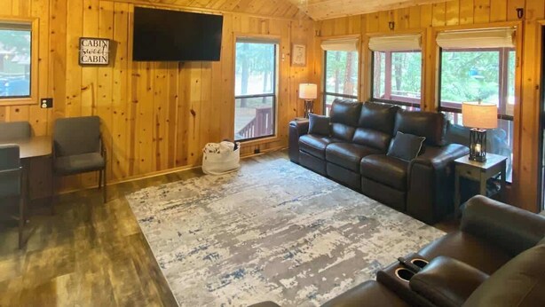 Een interieur van een blokhut met houten plafond, een bank, een eettafel met stoelen en een televisie.
