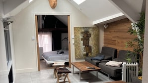 Un appartement moderne de style « loft », doté d’un plafond haut, d’une verrière et d’un coin salon confortable avec un canapé et une table basse.