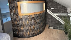 Une salle de bain moderne avec une douche, un meuble-lavabo avec un miroir et un mur décoratif orné d’un motif de feuilles.
