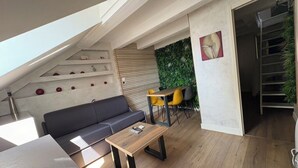 Une chambre moderne de style loft, dotée d’un plafond en pente, d’un canapé gris, d’une table basse en bois, d’une chaise jaune et d’un mur vert agrémenté d’un jardin vertical.