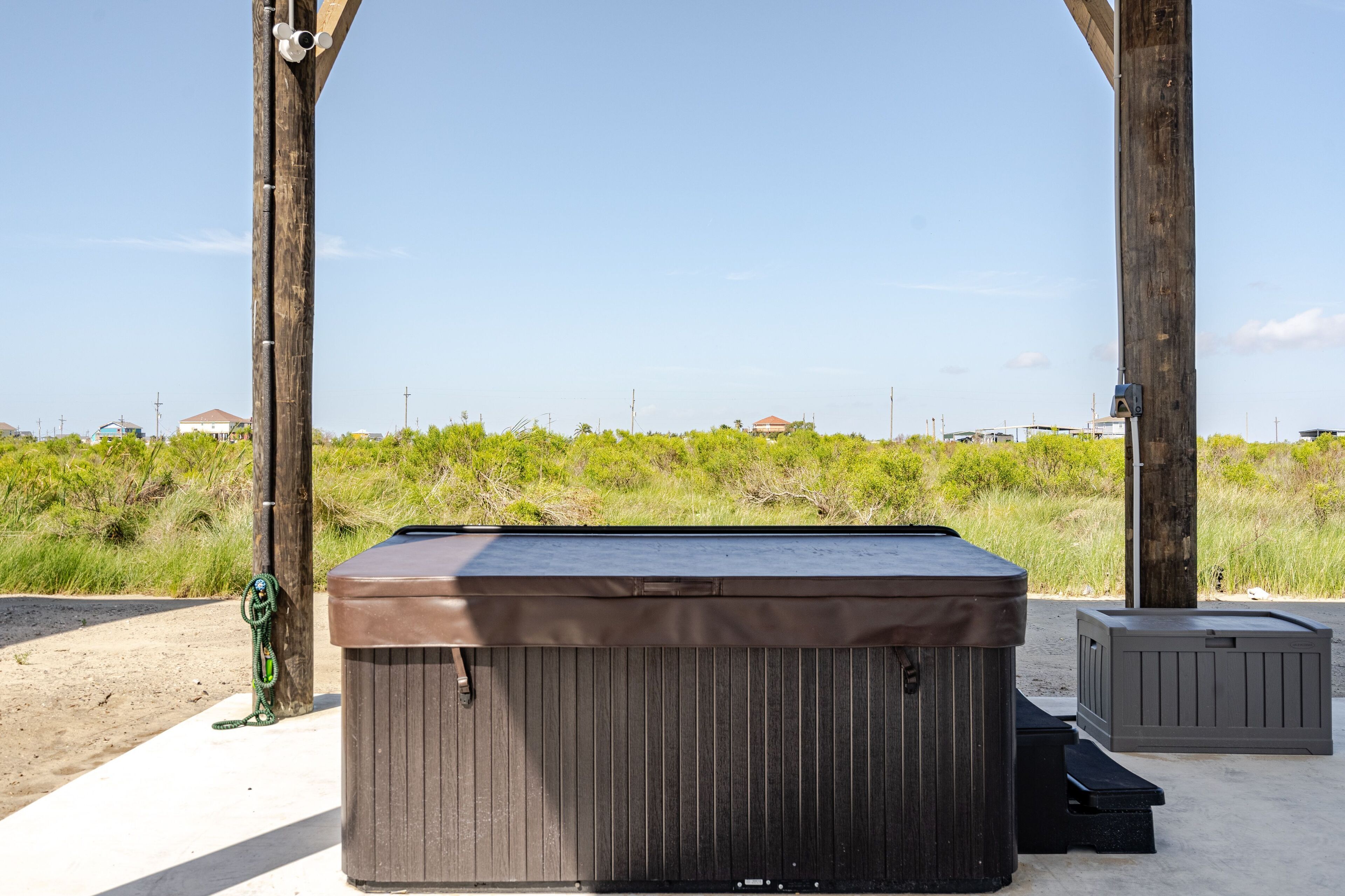 A hot tub under a wooden structure with a clear view of the beach and vegetation in the background.