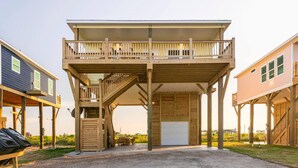 A two-story wooden structure with a balcony, a covered area, and a garage. - High Noon - Hot Tub, Golf Cart, Dog Friendly! (Bolivar Peninsula)