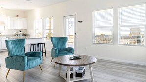 A modern living room with teal chairs, a wooden coffee table, and a view of the city through large windows. - High Noon - Hot Tub, Golf Cart, Dog Friendly! (Bolivar Peninsula)