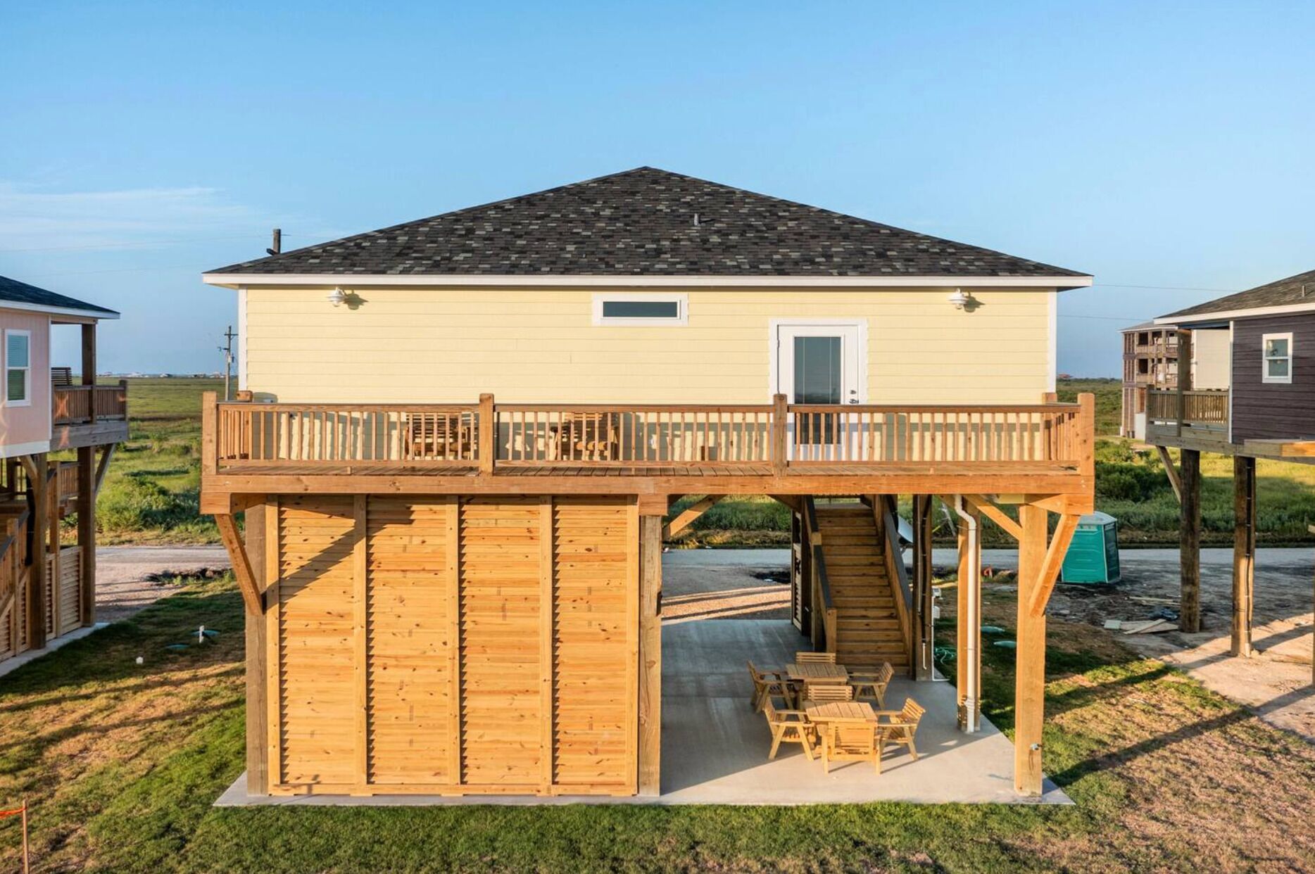 A two-story wooden structure with a balcony, a covered patio area with outdoor furniture, and a view of the surrounding landscape.