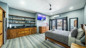 Habitación de hotel moderna con cama, kitchenette, televisor de pantalla plana y vista al área de la piscina.