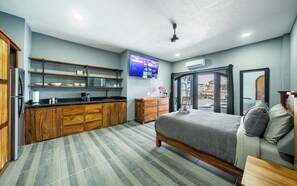 Ein modernes Hotelzimmer mit Bett, einer Küchenzeile, einem Flachbildfernseher und Blick auf den Poolbereich.