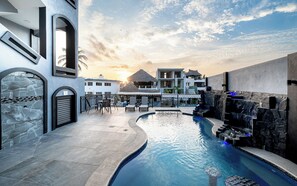 A pool area with a curved design, a thatched-roof structure, and a stone wall with a water feature. - Modern Apartment in the Heart of Barra de Navid (Barra de Navidad)