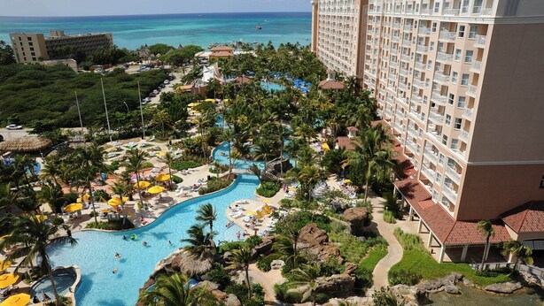 Un resort con una gran piscina, palmeras y vistas al océano.