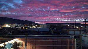A view of a town at dusk with a pink and purple sky, buildings, and a mountain in the background. - Creative Industrial Retreat with Decks, Games, Hot Tub & Spray Paint Trailer (Albuquerque)