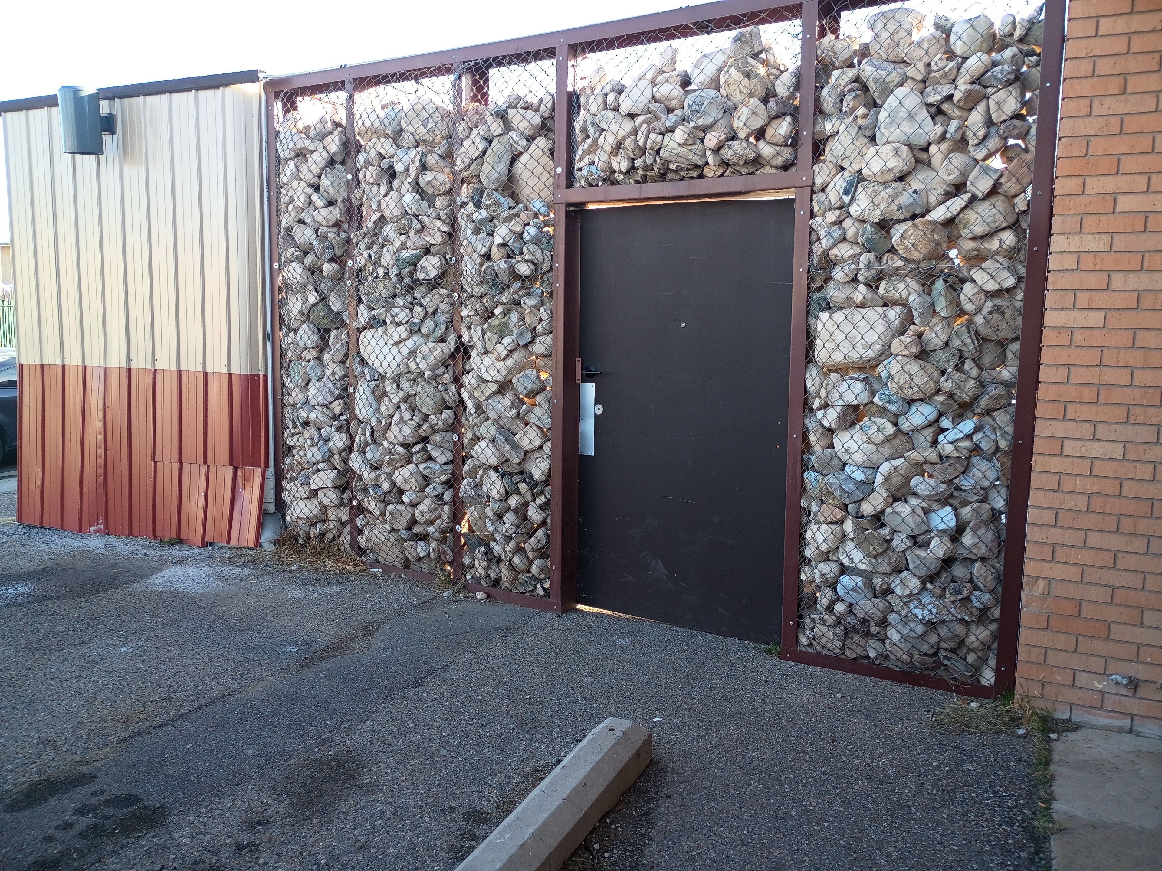 A building with a metal fence, a wooden door, and a gravel ground.