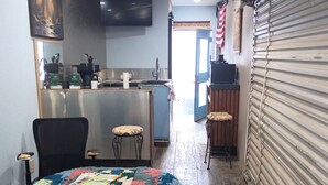 A kitchen area with a wooden table covered by a colorful quilt, a sink, and a television mounted on the wall. - Creative Industrial Retreat with Decks, Games, Hot Tub & Spray Paint Trailer (Albuquerque)