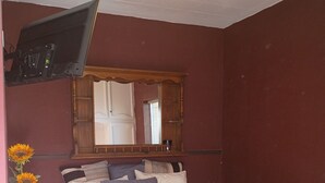 A bedroom with a bed, a television mounted on the wall, a ceiling fan, and a mirror above the bed. - Creative Industrial Retreat with Decks, Games, Hot Tub & Spray Paint Trailer (Albuquerque)