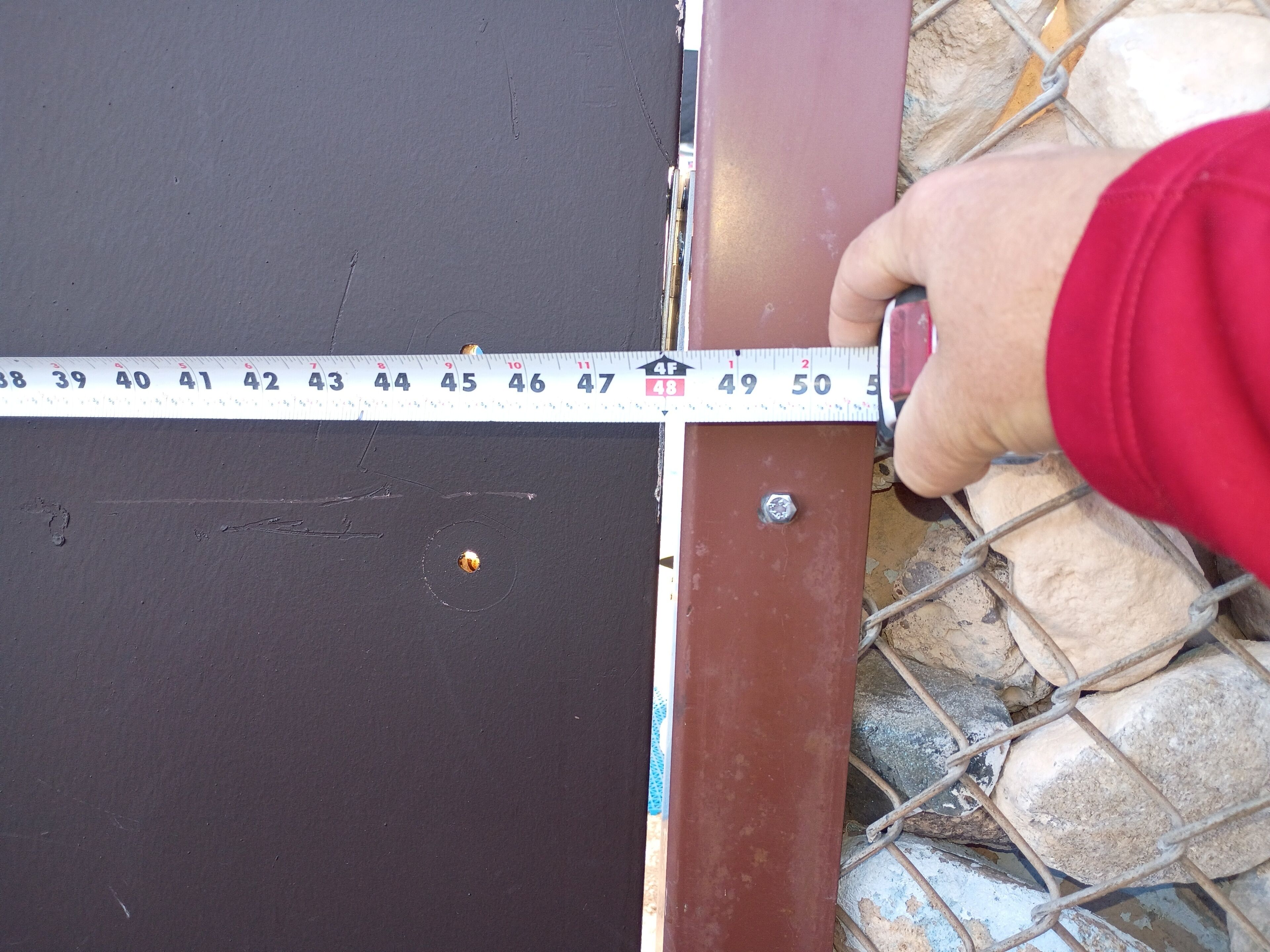 On utilise un mètre ruban pour mesurer une structure métallique par rapport à un mur en pierre.