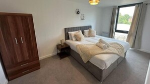 A bedroom with a large bed, a wardrobe, a bedside table, and a window with curtains. - Chic York Apartment - Free Parking & Gym Access (York)
