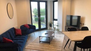 A modern living room with a sofa, coffee table, dining table, chairs, and a TV. - Chic York Apartment - Free Parking & Gym Access (York)