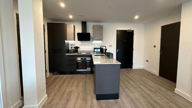 A modern kitchen with a central island, built-in appliances, and a flat-screen TV. - Chic York Apartment - Free Parking & Gym Access (York)