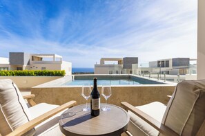 A rooftop terrace with a pool, two lounge chairs, a table with a bottle of wine and two glasses, and a view of the sea and buildings. - Brisa Del Sol - Cabo Costa (Cabo San Lucas)