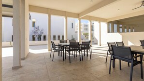 A spacious outdoor patio with a dining area, large windows, and a view of the surrounding buildings. - Brisa Del Sol - Cabo Costa (Cabo San Lucas)