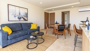 A modern living room with a blue sofa, a coffee table, and a dining area with wooden chairs and a table. - Brisa Del Sol - Cabo Costa (Cabo San Lucas)