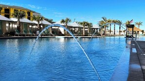 Una piscina con fuentes, sillas de descanso y palmeras.