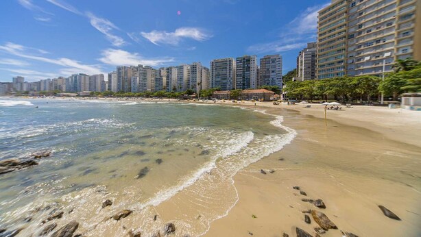 A beach with clear waters, a sandy shore, and high-rise buildings in the background. - Apto c Piscina, Garagem e Academia a 180m da Praia (Guarujá)